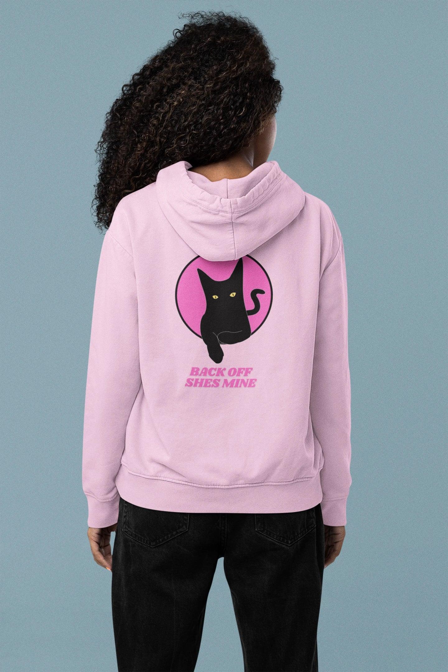 Person wearing a pink hoodie with a black cat graphic and text on the back against a gray background