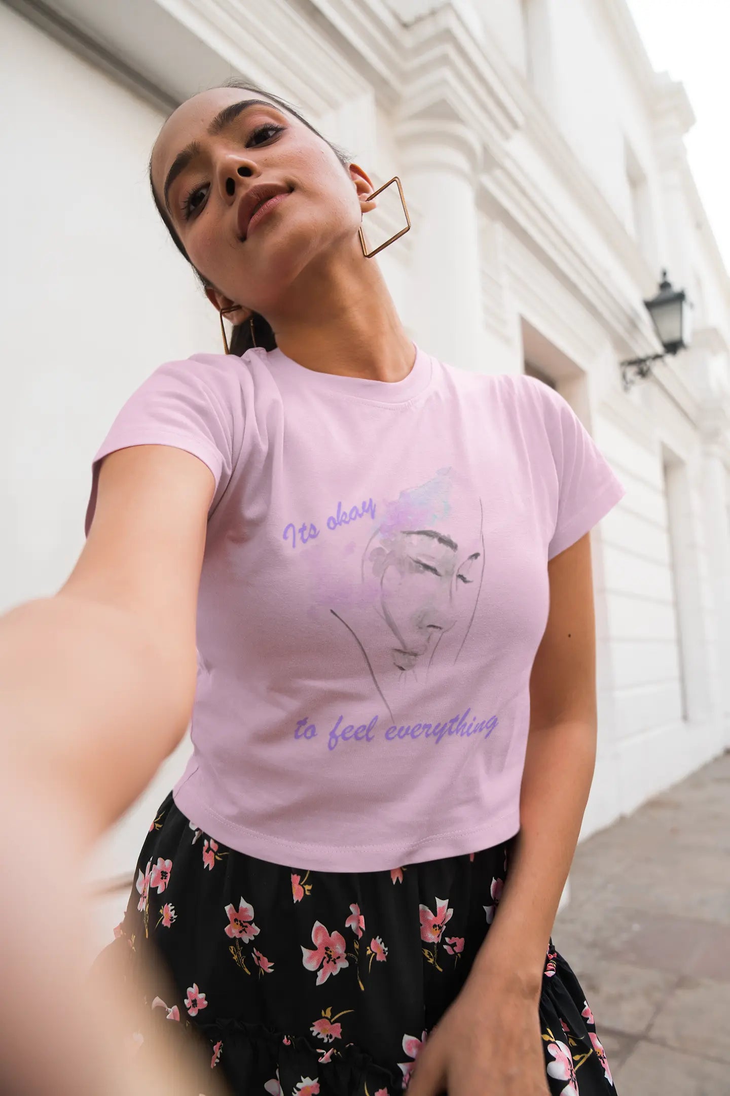 Woman wearing a pink t-shirt with text and graphics, standing outdoors.