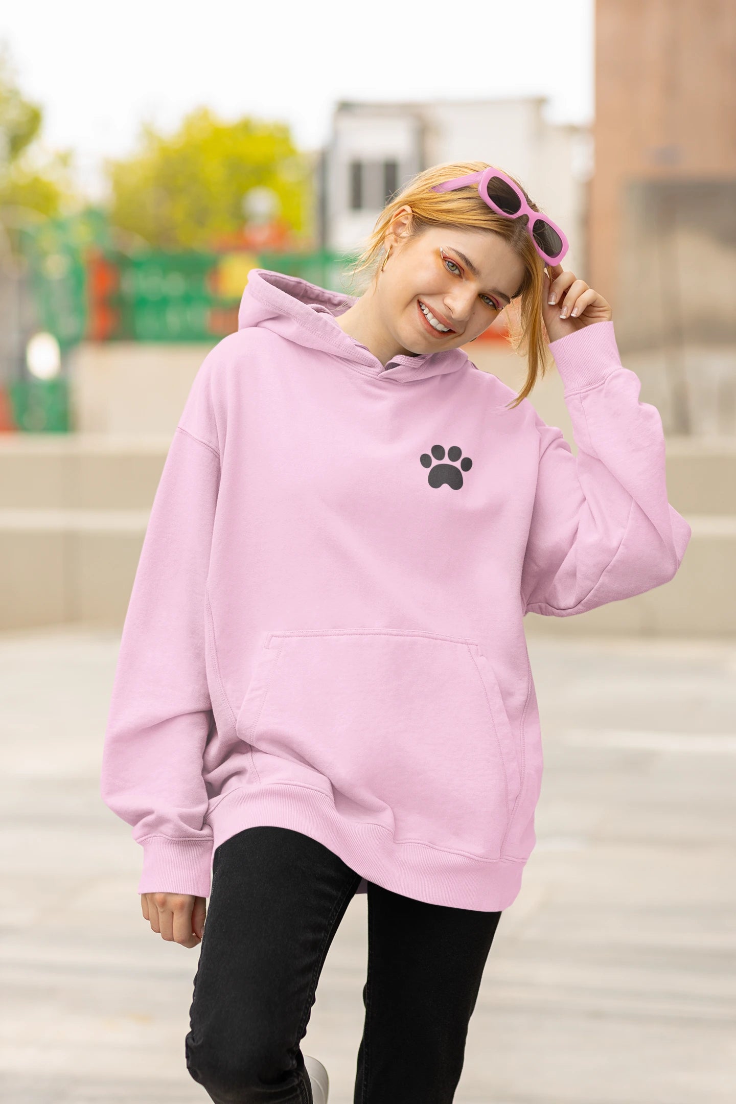 Person wearing a pink hoodie with a paw print design outdoors.