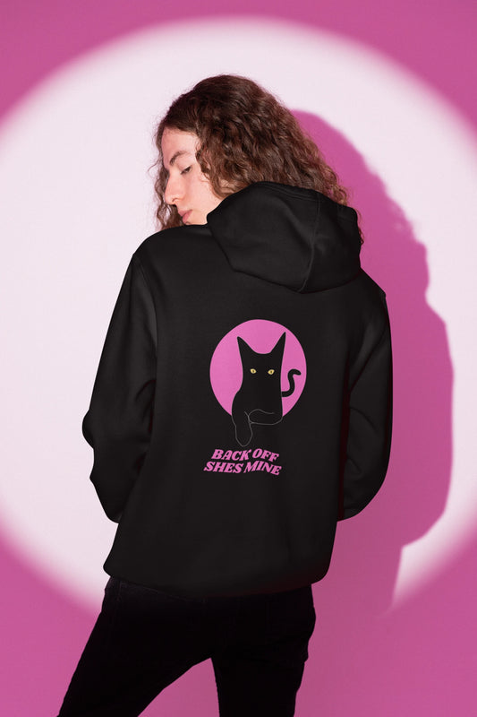 Person wearing a black hoodie with a cat graphic and text on the back against a pink and white abstract background