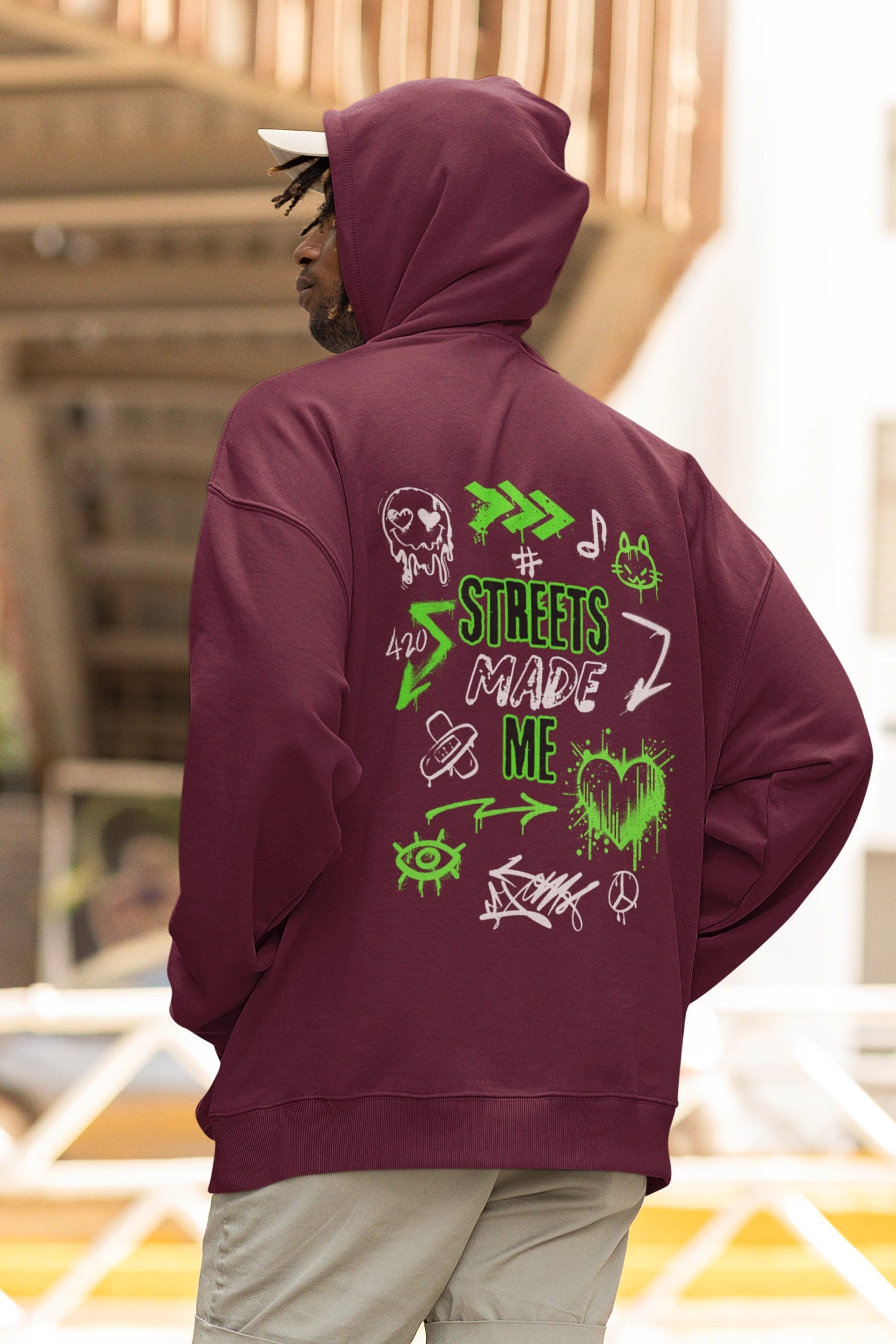 Person wearing a maroon hoodie with green graphics and text on the back, standing in an outdoor setting.