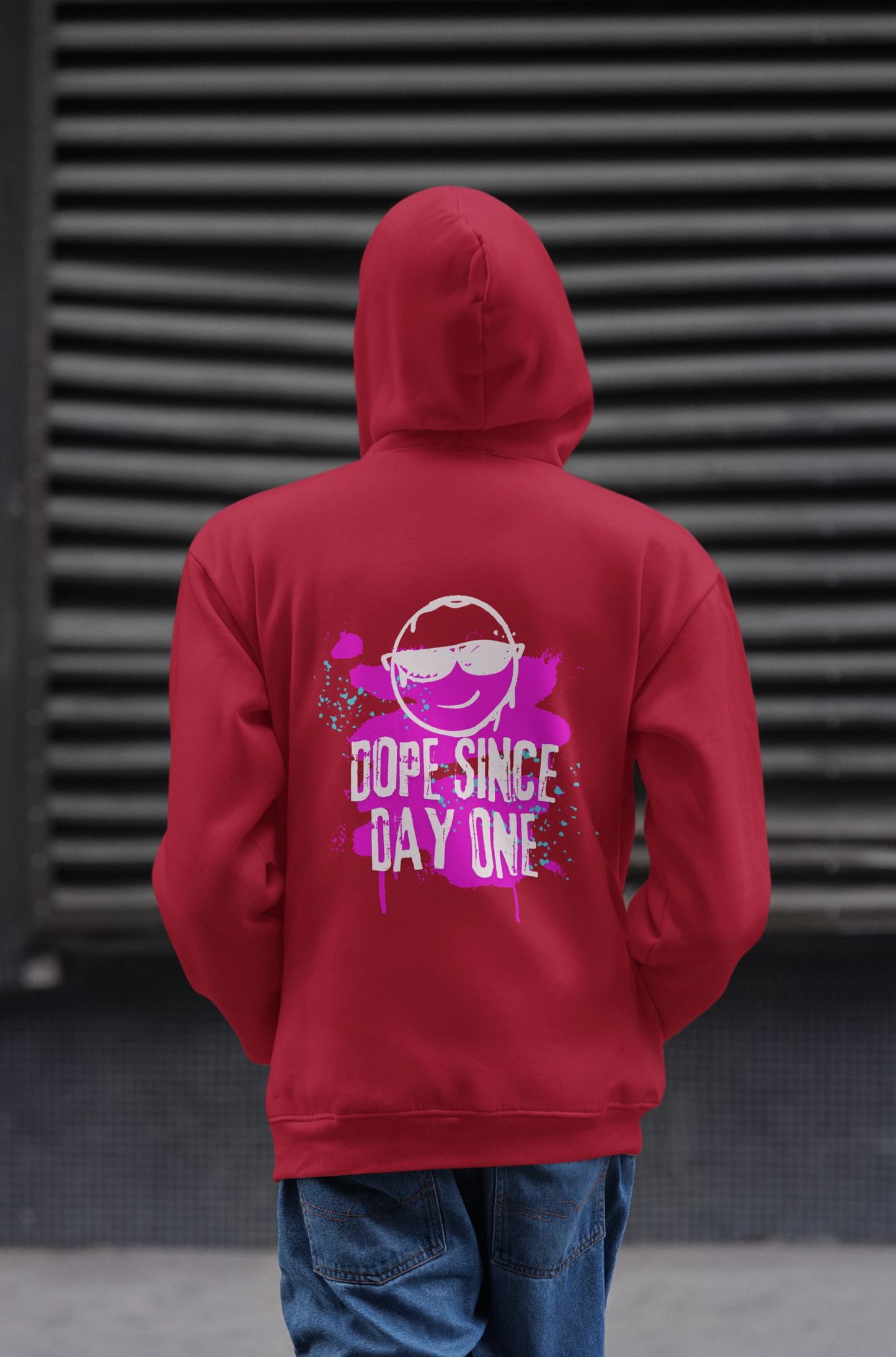 Person wearing a red hoodie with a graphic and text on the back, standing against a dark textured wall.