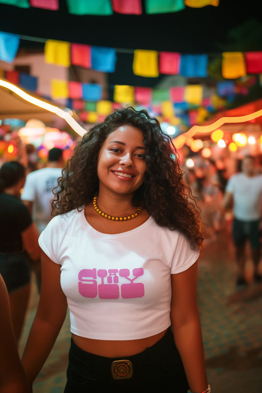 Woman wearing a white t-shirt with pink text at a festive outdoor event.