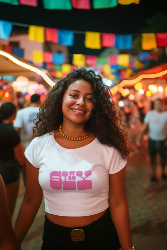 Woman wearing a white t-shirt with pink text in a festive outdoor setting with colorful flags.