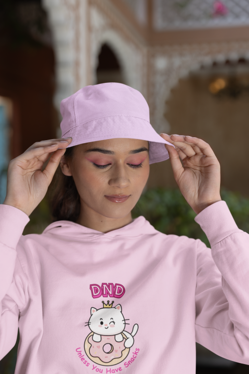 Person wearing a pink hoodie with a cat graphic and text, adjusting a matching pink bucket hat.