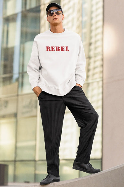 Person wearing a white sweatshirt with 'REBEL' printed in red, black pants, and black shoes, standing against a modern building.